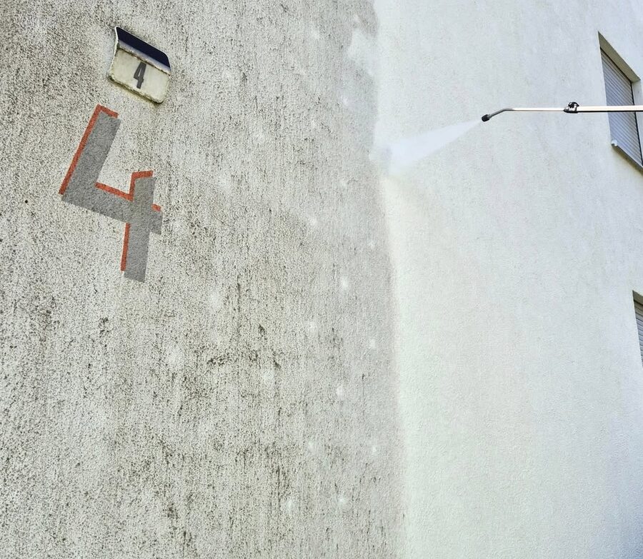 Nahaufnahme des Wasserstrahls an der Fassade, scharfe Kante zwischen verschmutztem und gereinigtem Putz