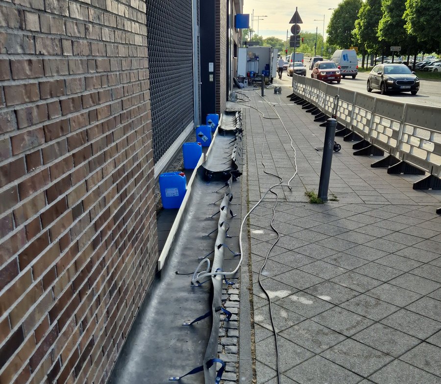 Gesicherter Gehweg an der Baustelle: Absperrgitter, verlegte Schläuche und Kanister entlang der Fassade