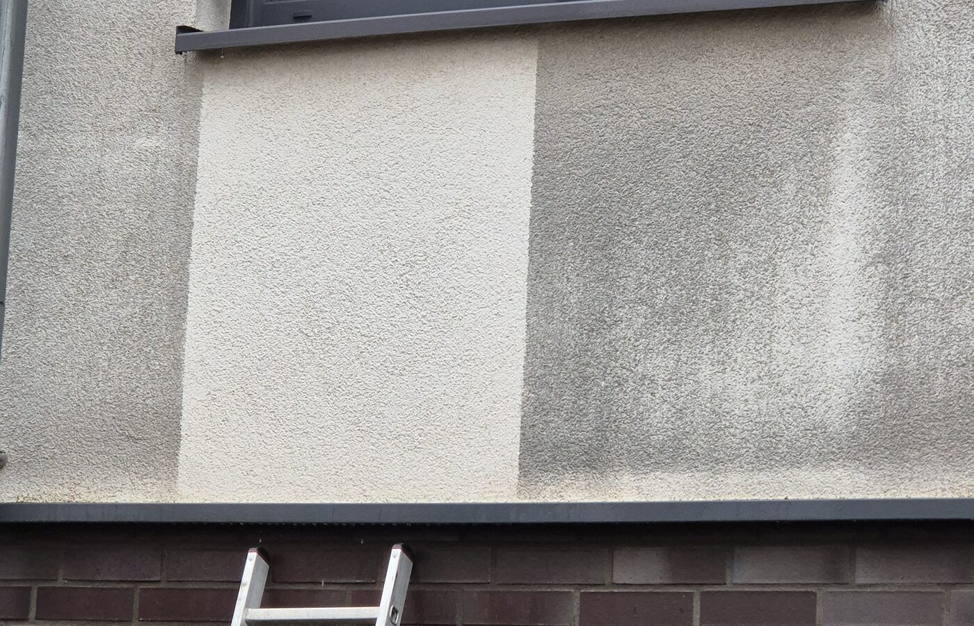 Probefläche an der Fassade: der gereinigte Bereich hebt sich hell vom Rest der Wand ab